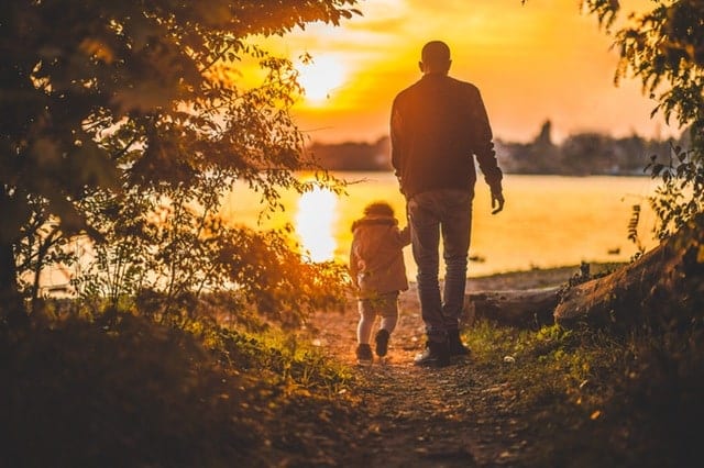 A father walking holding the hand of his son, sunset in the background